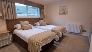 Ein Schlafzimmer mit zwei Betten, einem Nachttisch, einem Heizkörper und einem Fenster mit Vorhängen.