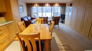 A spacious living area with a wooden dining table, chairs, and a sofa. There is a television and a window with curtains. - Loch Rannoch Highland Club Studio 3 (Kinloch Rannoch)