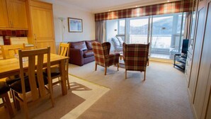 A cozy living room with a dining table, chairs, a sofa, and a large window with a view. - Loch Rannoch Highland Club Studio 3 (Kinloch Rannoch)