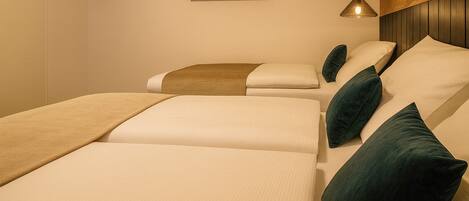 A room with three beds arranged in a row, each with a pillow and a blanket.