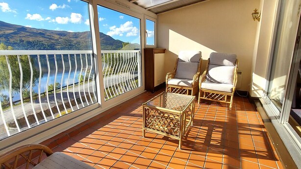 Ein Balkon mit Blick auf einen See und Berge, ausgestattet mit Korbmöbeln und einem kleinen Tisch.
