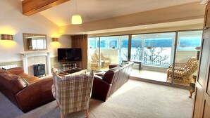 A spacious living room with a fireplace, a television, and a balcony with wicker furniture. - Loch Rannoch Highland Club, Grouse Lodge (Kinloch Rannoch)