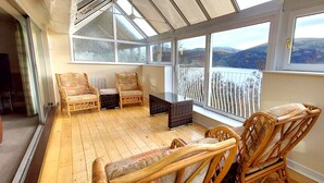 A sunroom with wicker furniture, large windows, and a view of hills. - Loch Rannoch Highland Club, Grouse Lodge (Kinloch Rannoch)