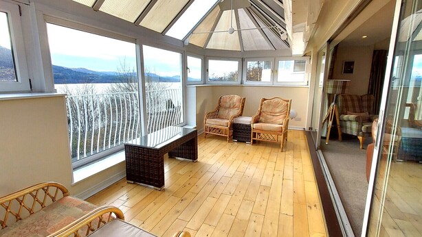 A sunroom with large windows, wicker furniture, and a view of a snowy landscape. - Loch Rannoch Highland Club, Grouse Lodge (Kinloch Rannoch)
