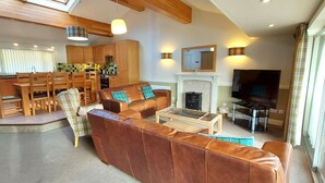 A spacious living area with a large brown leather sofa, a wooden dining table with chairs, a fireplace, and a television. - Loch Rannoch Highland Club, Grouse Lodge (Kinloch Rannoch)