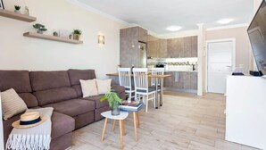 Una sala de estar moderna con un sofá marrón, una mesita auxiliar y una zona de comedor con sillas blancas y una mesa de madera.