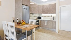 Una cocina compacta con refrigerador, microondas y horno. Hay una mesa de comedor con sillas y un frutero.