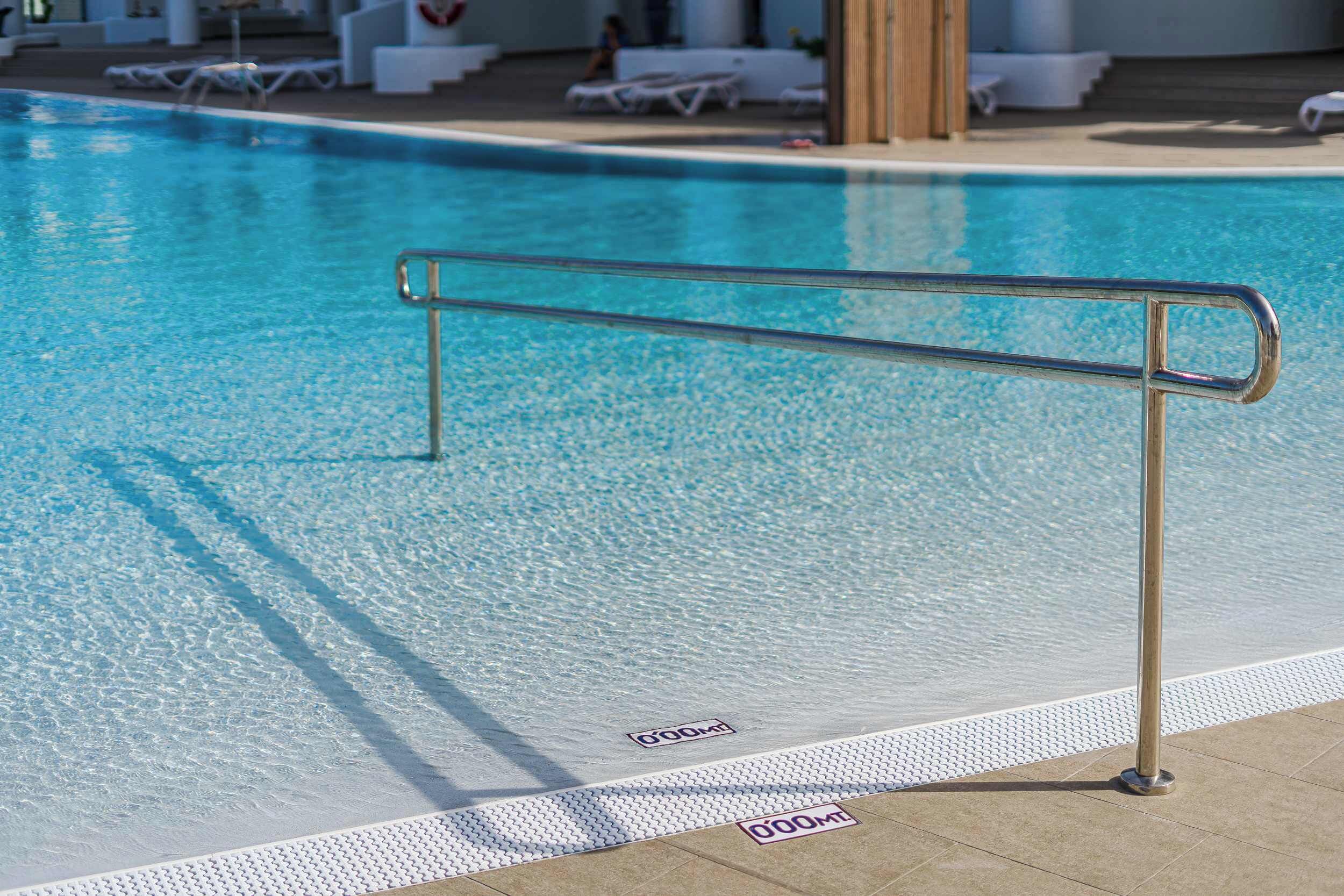 Una piscina con barandilla de seguridad metálica, un suelo de baldosas y una silla para socorristas.