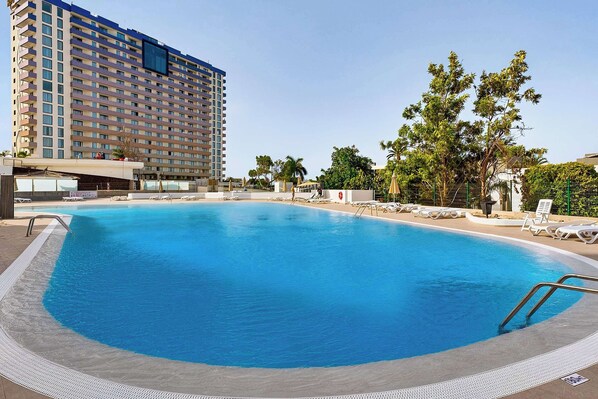 Un hotel con una piscina grande, sillas de descanso y palmeras.