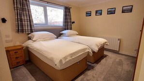 Un lit double avec une tête de lit en bois, une table de chevet avec des tiroirs, une fenêtre avec des rideaux à carreaux et un radiateur fixé au mur.