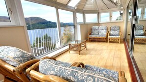 Un balcone baciato dal sole con mobili in vimini, un tavolino in vetro e vista su dolci colline.