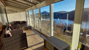 A covered outdoor seating area with wicker furniture and a view of a lake and mountains. - Loch Rannoch Highland Club, Highland Lodge 35 (Kinloch Rannoch)