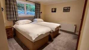 Ein Schlafzimmer mit zwei Einzelbetten, einem hölzernen Nachttisch, einem Heizkörper und zwei gerahmten Bildern an der Wand.