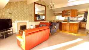 A living room with a fireplace, a television, a red sofa, and a kitchen area with wooden cabinets.