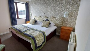 A bedroom with a bed, bedside tables, a window with curtains, and a radiator.