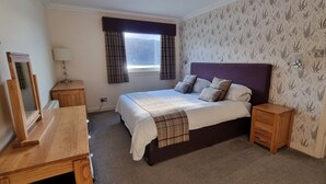 A bedroom with a bed, bedside tables, a dresser, a window with curtains, and patterned wallpaper.
