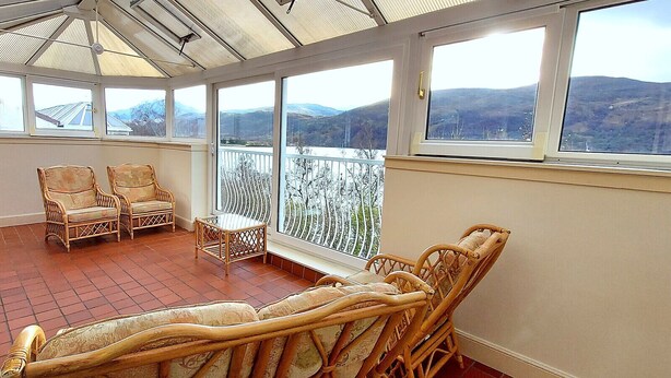 A sunroom with wicker furniture, large windows, and a view of mountains.
