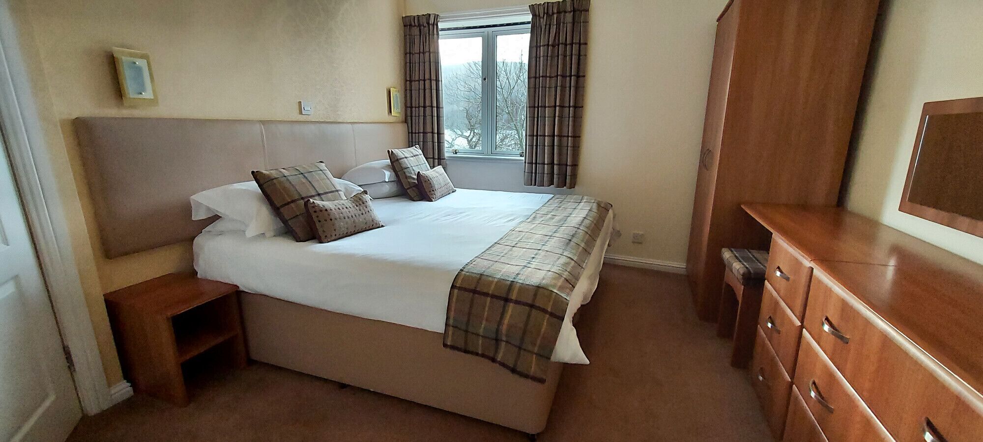 A bedroom with a large bed, a wooden dresser, and a window with curtains.