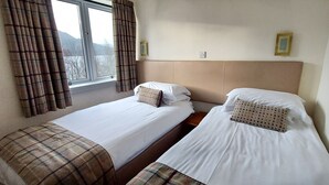 A twin room with two beds, a window with curtains, and a view of the outside.