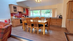 A modern kitchen with wooden cabinets, a dining table with chairs, and a view of a green landscape through the window.