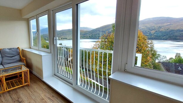 A balcony with a wicker sofa and a small table, overlooking a lake and hills. - Loch Rannoch Highland Club,  Red Deer 5 (Kinloch Rannoch)