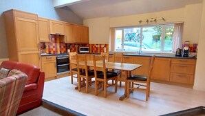 Une cuisine de taille réduite avec des meubles en bois, une table à manger avec des chaises, un canapé rouge et une fenêtre donnant sur l’extérieur.