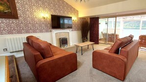 A living room with two brown leather sofas, a small wooden table, a fireplace, and a TV mounted on the wall. - Loch Rannoch Highland Club, Highland Lodge 36 (Kinloch Rannoch)