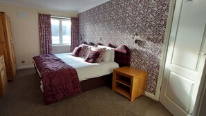 A bedroom with a bed, wooden dresser, and patterned wallpaper. - Loch Rannoch Highland Club, Highland Lodge 36 (Kinloch Rannoch)