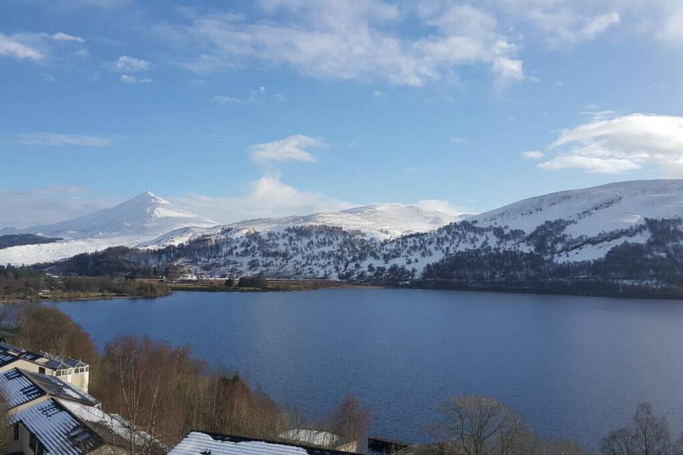 En sø omgivet af sneklædte bjerge og enkelte bygninger med tagrygge.