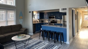 A modern kitchen with dark blue cabinets, a stainless steel refrigerator, and a built-in oven. There is a dining area with a round table and bar stools. - Sleep 8 in this guest fave! All new, fresh & fun!walk to lake and marina. (Holiday Island)