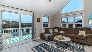 A spacious living room with a large brown sectional sofa, a ceiling fan, and a view of the outdoors through large sliding glass doors. - Sleep 8 in this guest fave! All new, fresh & fun!walk to lake and marina. (Holiday Island)