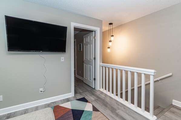 A hallway with a flat-screen TV mounted on the wall, a white railing, and a patterned rug on the floor. - Sleep 8 in this guest fave! All new, fresh & fun!walk to lake and marina. (Holiday Island)