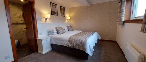 A bedroom with a bed, bedside tables, a nightstand, a window with curtains, and a wall with a patterned wallpaper.