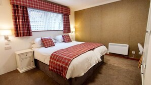 A bedroom with a bed, a nightstand, a window with curtains, a wall-mounted heater, and a bedside lamp. - Loch Rannoch Highland Club, Otter Lodge 3 (Kinloch Rannoch)