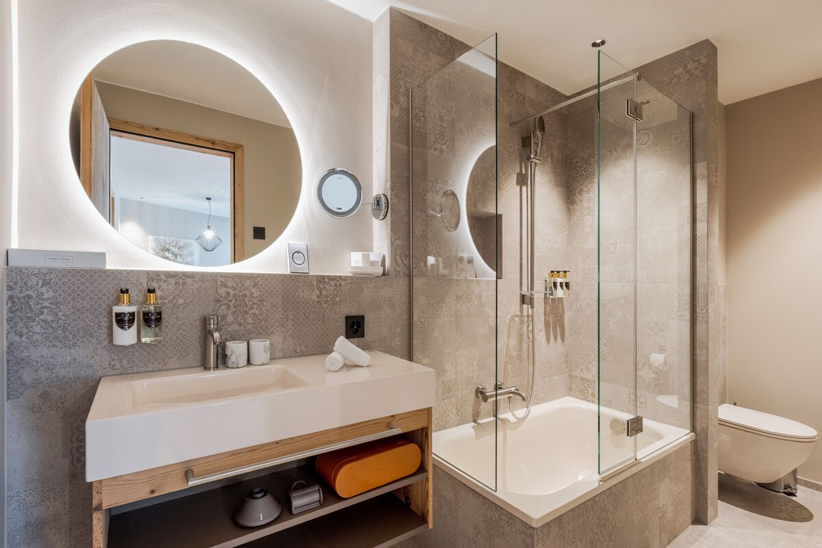 A modern bathroom with a large mirror, a glass-enclosed shower, and a white sink.