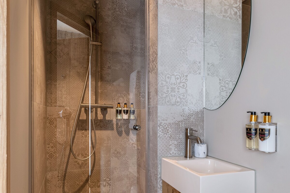Un baño moderno con ducha envuelta en vidrio, tocador de madera y un espejo grande.