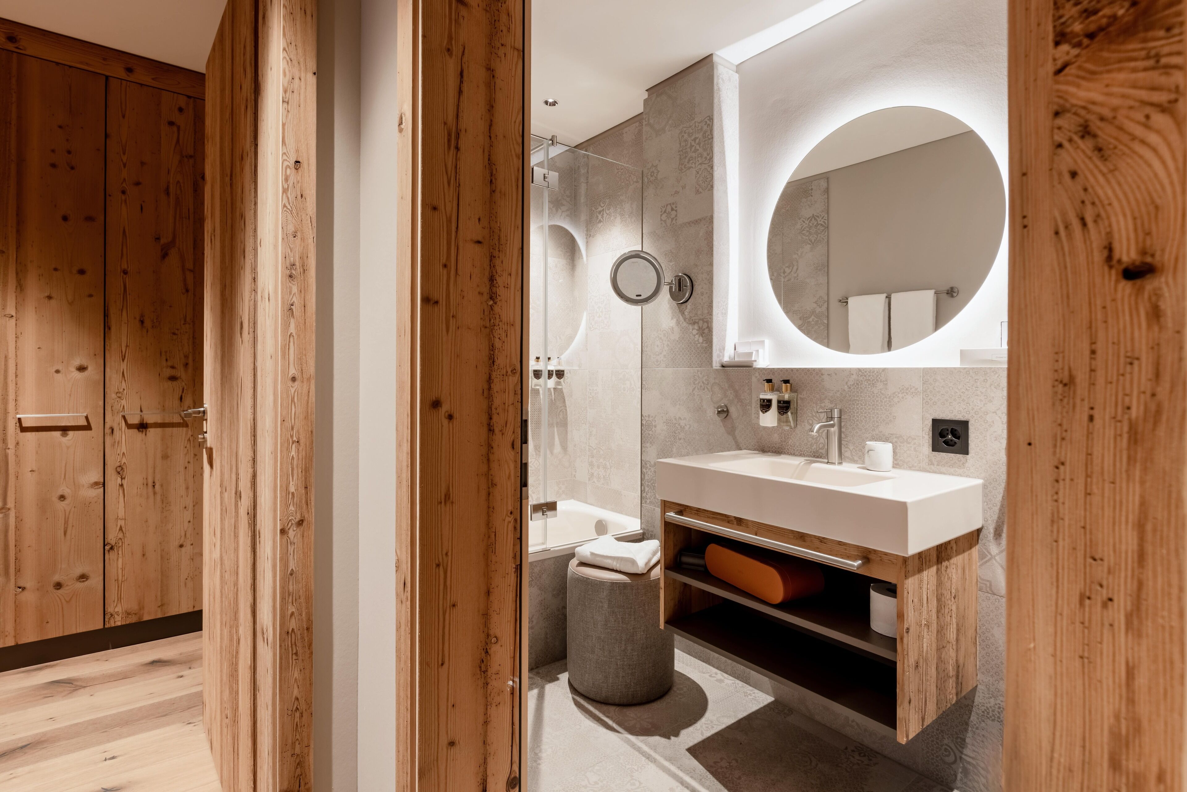 A modern bathroom with a wooden vanity, a round mirror, and a bathtub.