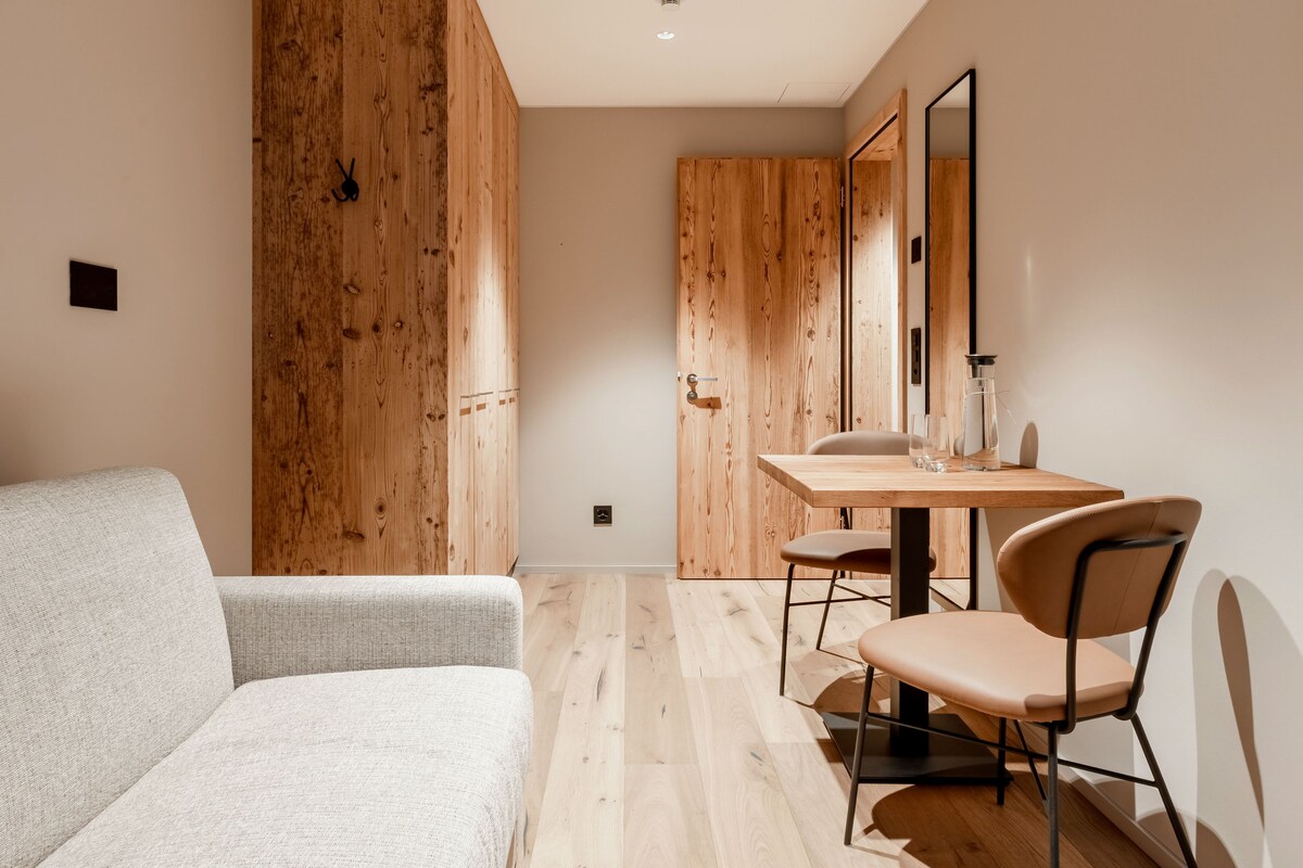 Una habitación moderna con un armario de madera, un sofá, una mesa de comedor con sillas y un espejo en la pared.
