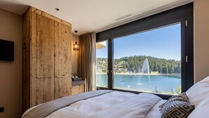 A bedroom with a large window, a wooden wardrobe, and a bed with white bedding. - Postresidenz am See (Arosa)