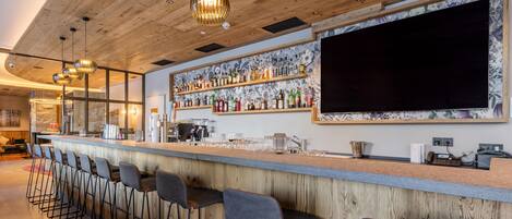 A bar area with wooden ceiling, bar stools, and a wall-mounted TV.