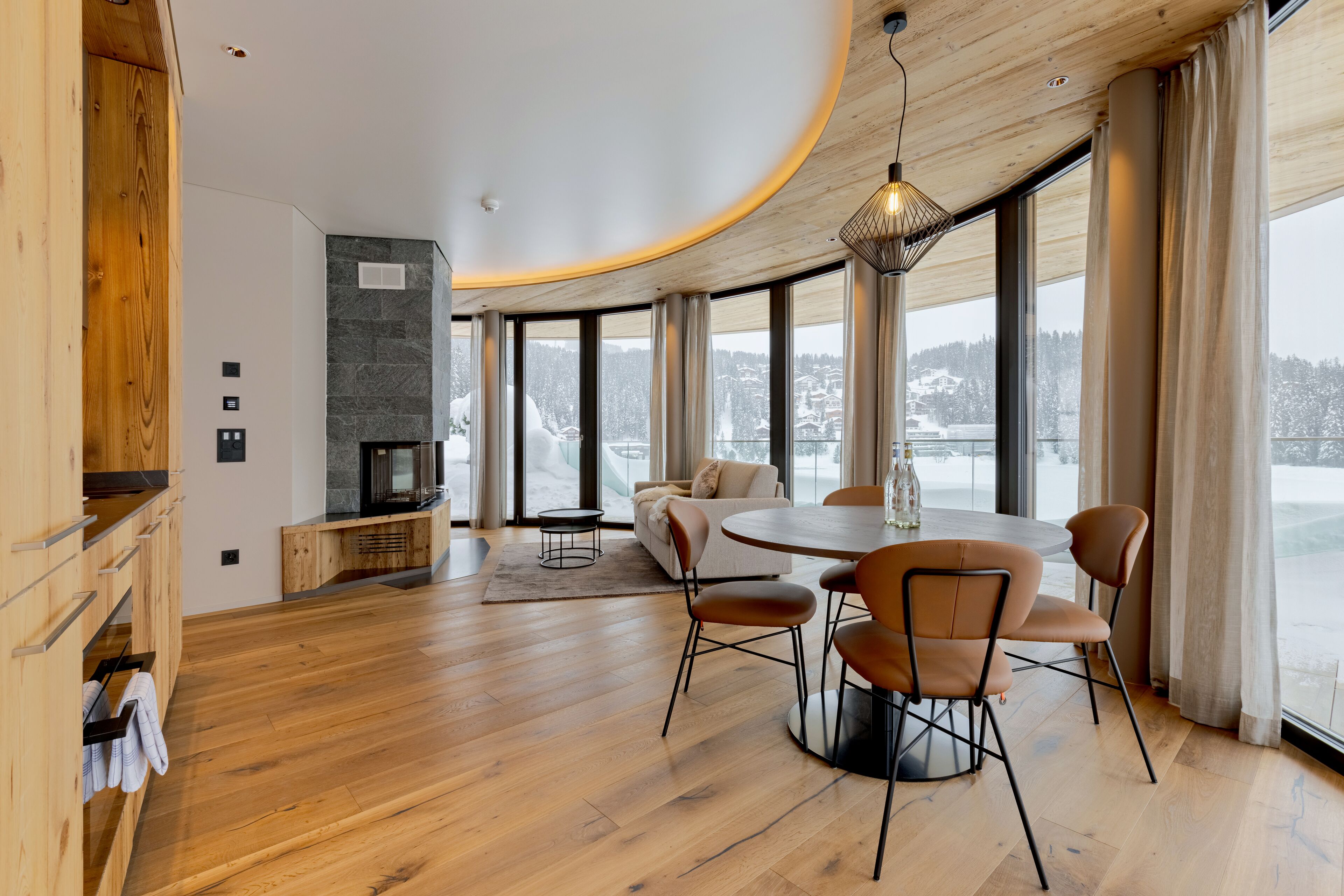 A modern interior with a wooden floor, a round dining table with chairs, a sofa, and a fireplace.