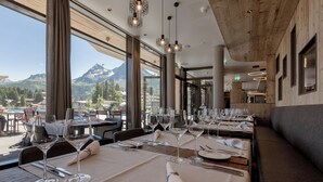 A restaurant with tables set for dining, large windows with a mountain view, and hanging pendant lights. - Postresidenz am See (Arosa)