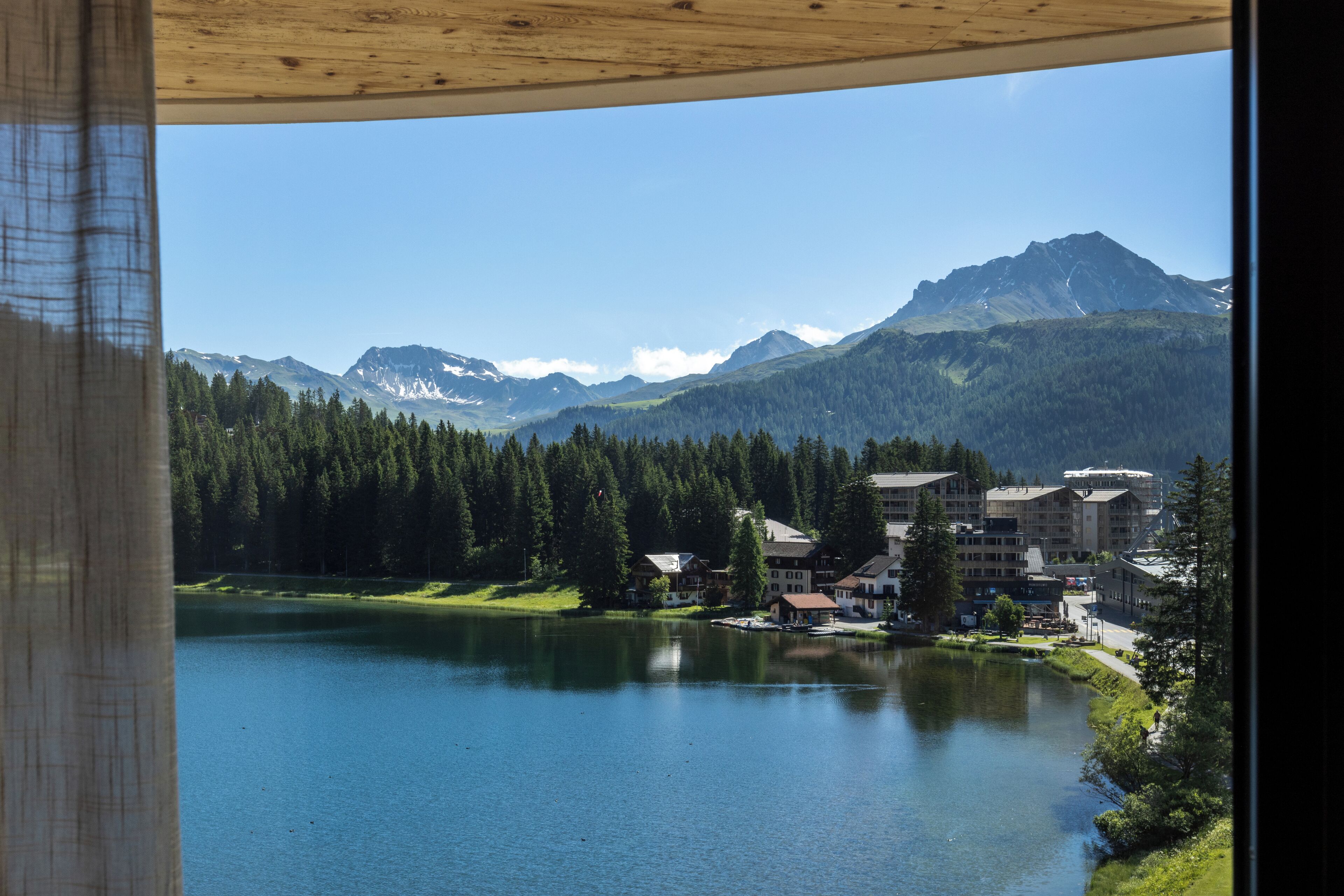 A lake with a mountain range in the background, surrounded by buildings and trees.