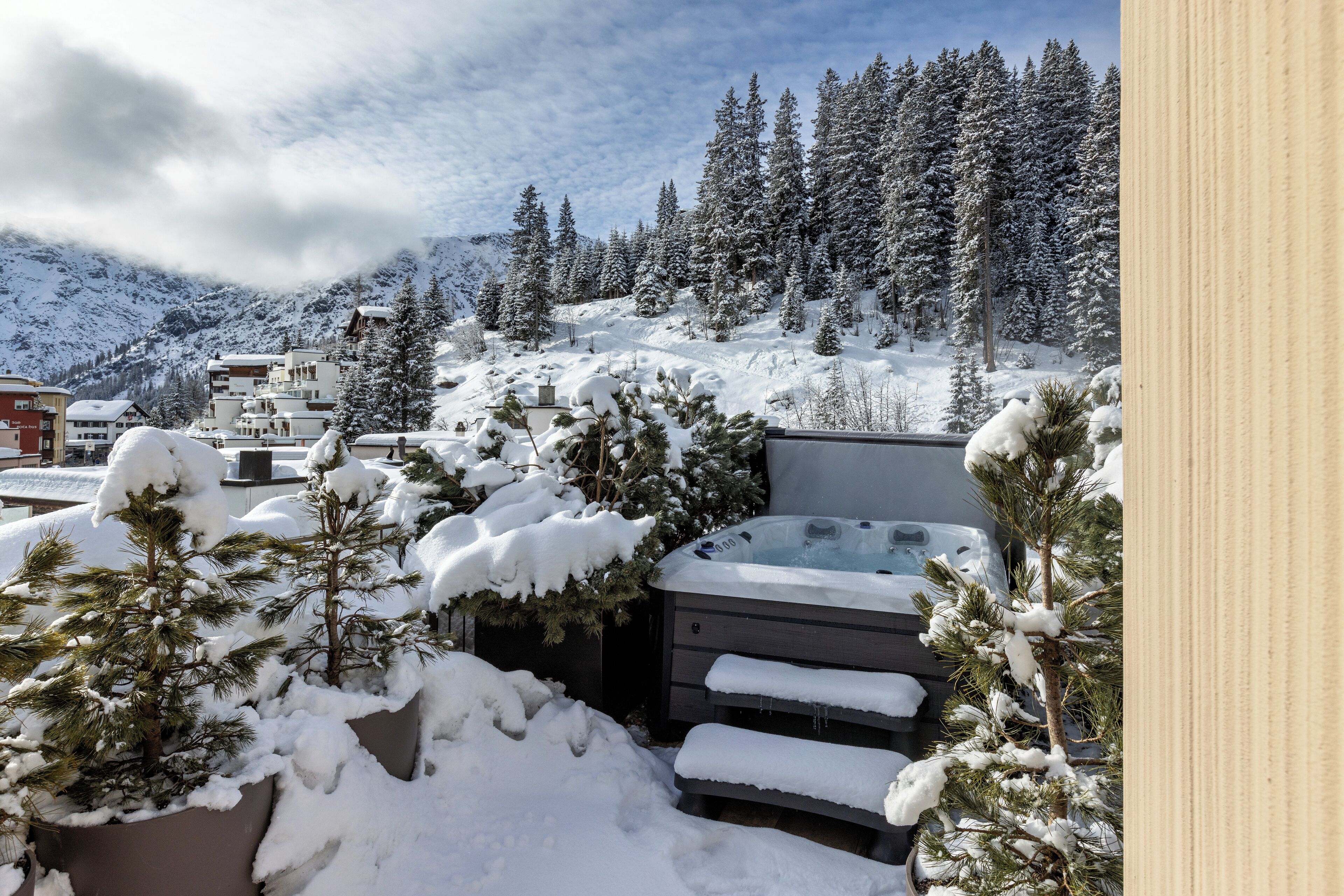 A snowy outdoor area with a hot tub surrounded by snow-covered trees and buildings.