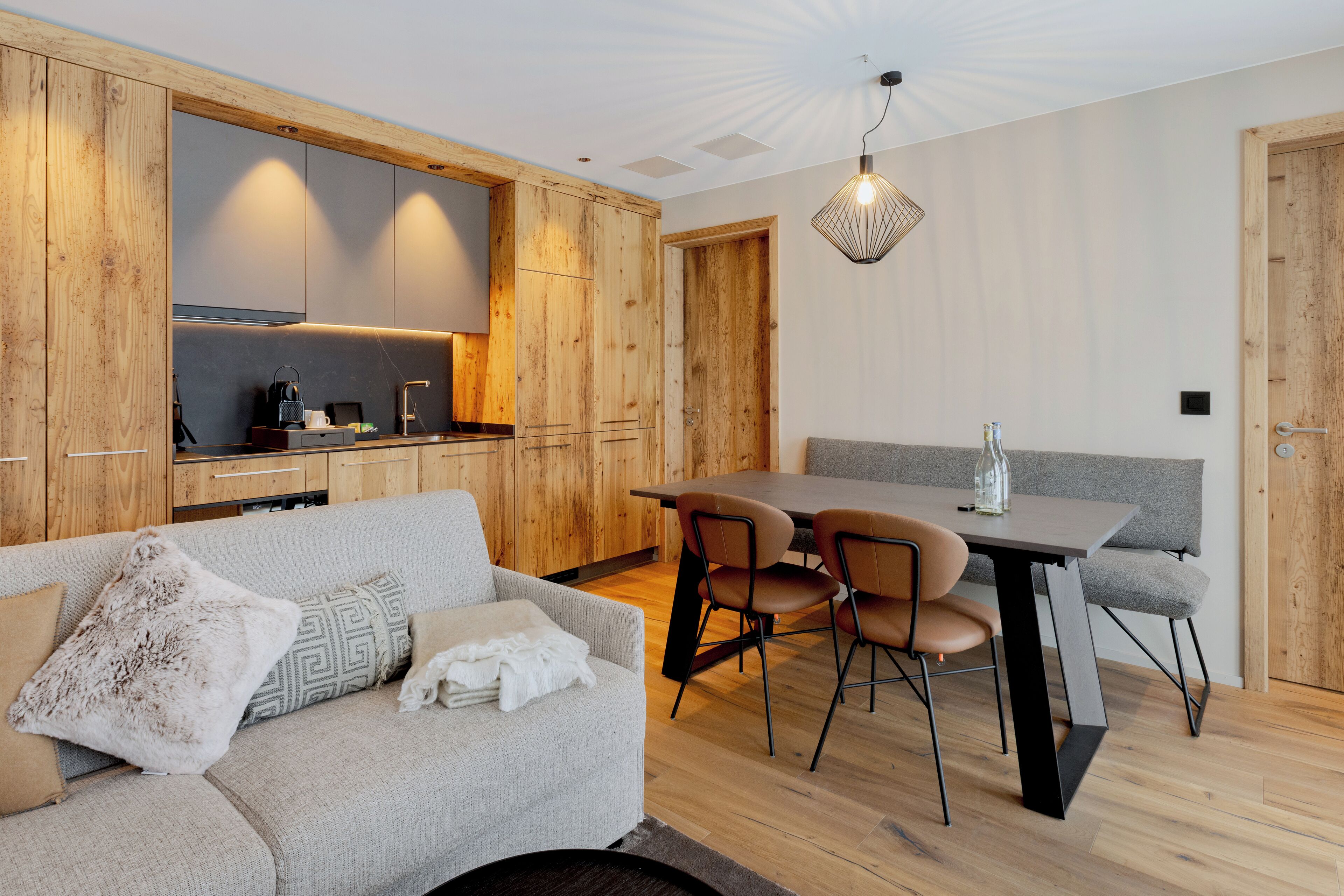 A modern kitchen with wooden cabinets, a dining area with a table and chairs, and a cozy seating area with a sofa.
