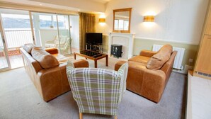 A spacious living room with a fireplace, a television, and a view of the outdoors through large windows.