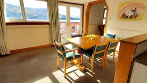 A dining area with a wooden table and chairs, a view of the outdoors through a window, and a painting on the wall.