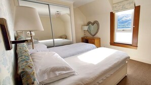 A bedroom with two beds, a mirror, a nightstand, a chair, and a window with a view.
