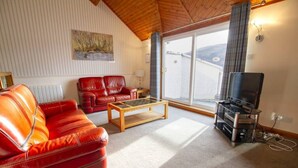 Een woonkamer met een rode leren bank, een houten salontafel en een tv-meubel met een flatscreen televisie.