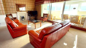 A living room with a fireplace, a television, and a large window overlooking a balcony. - Loch Rannoch Highland Club, Highland Lodge 8 (Kinloch Rannoch)